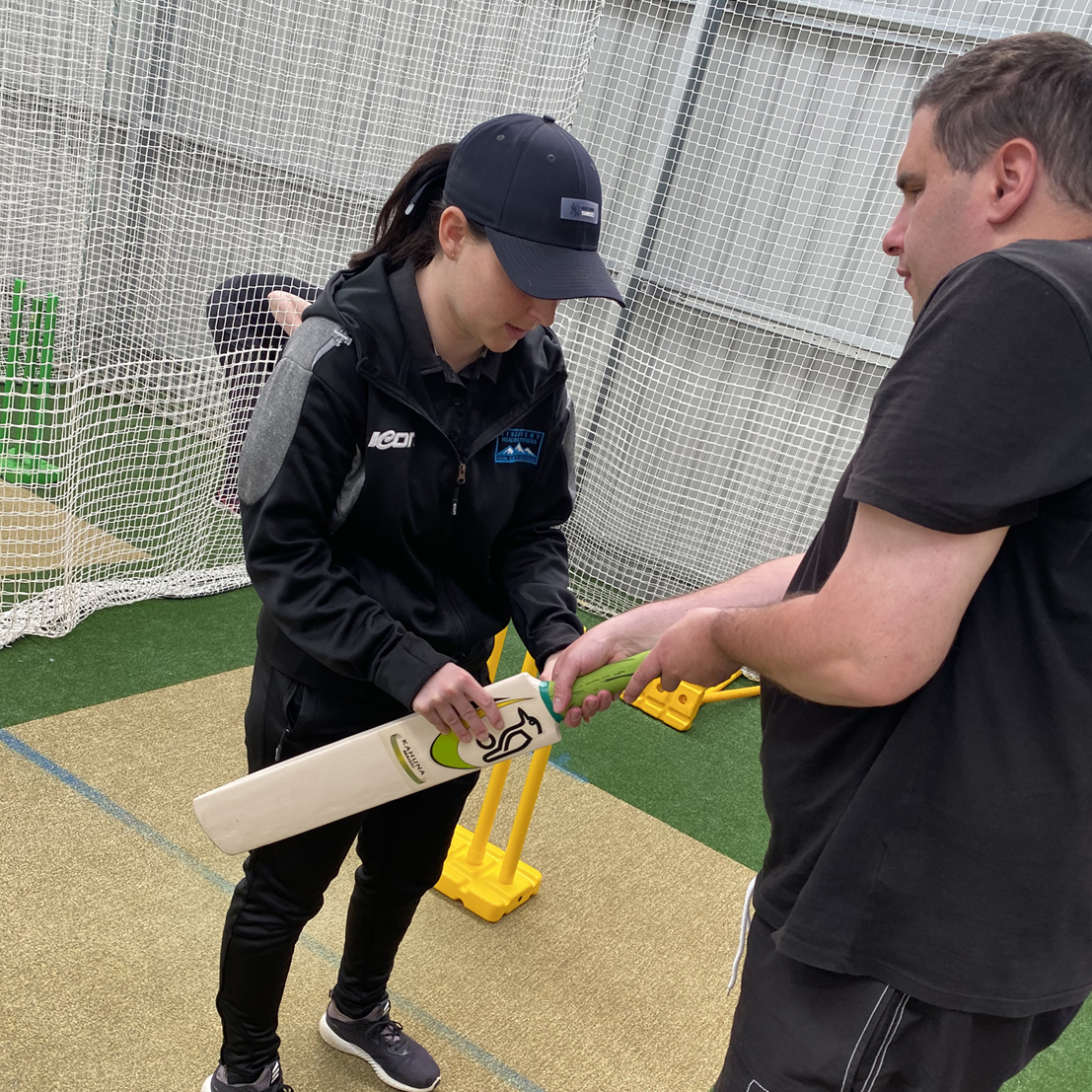 Head Coach Taylah Purton showing a B1 blind player how to grip the bat in an indoor train g session