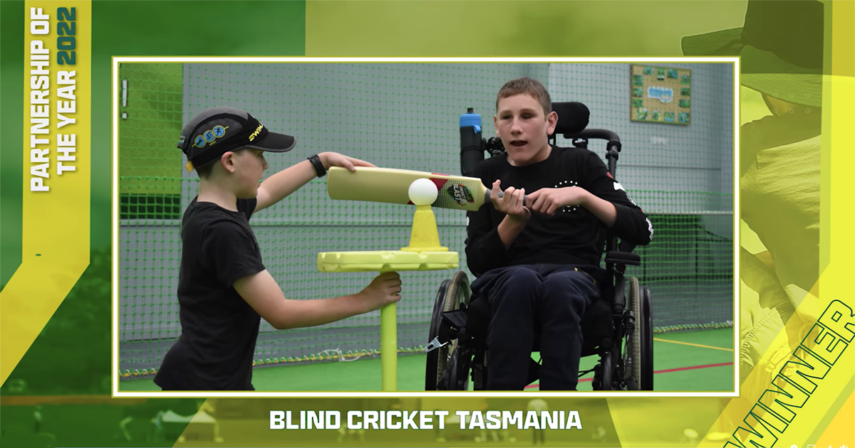 A young boy who is totally blind and a wheelchair user is assisted to play blind cricket with adaptive equipment that allows him to join in the game with others