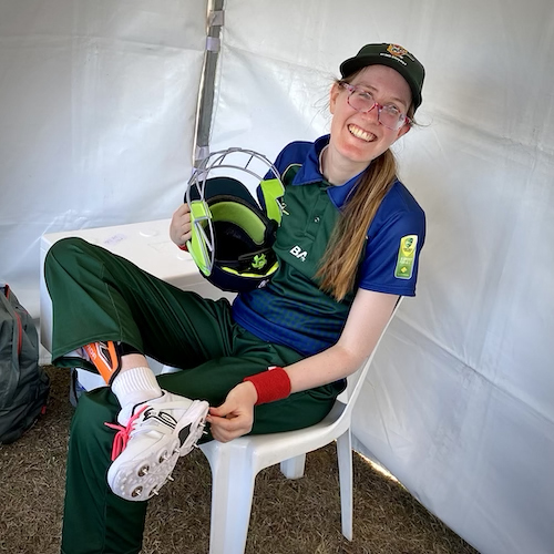 Nicole McKillop sitting in the team tent holding her helmet and ready to take the field. She has a big smile indicating how proud and happy she is playing in the team