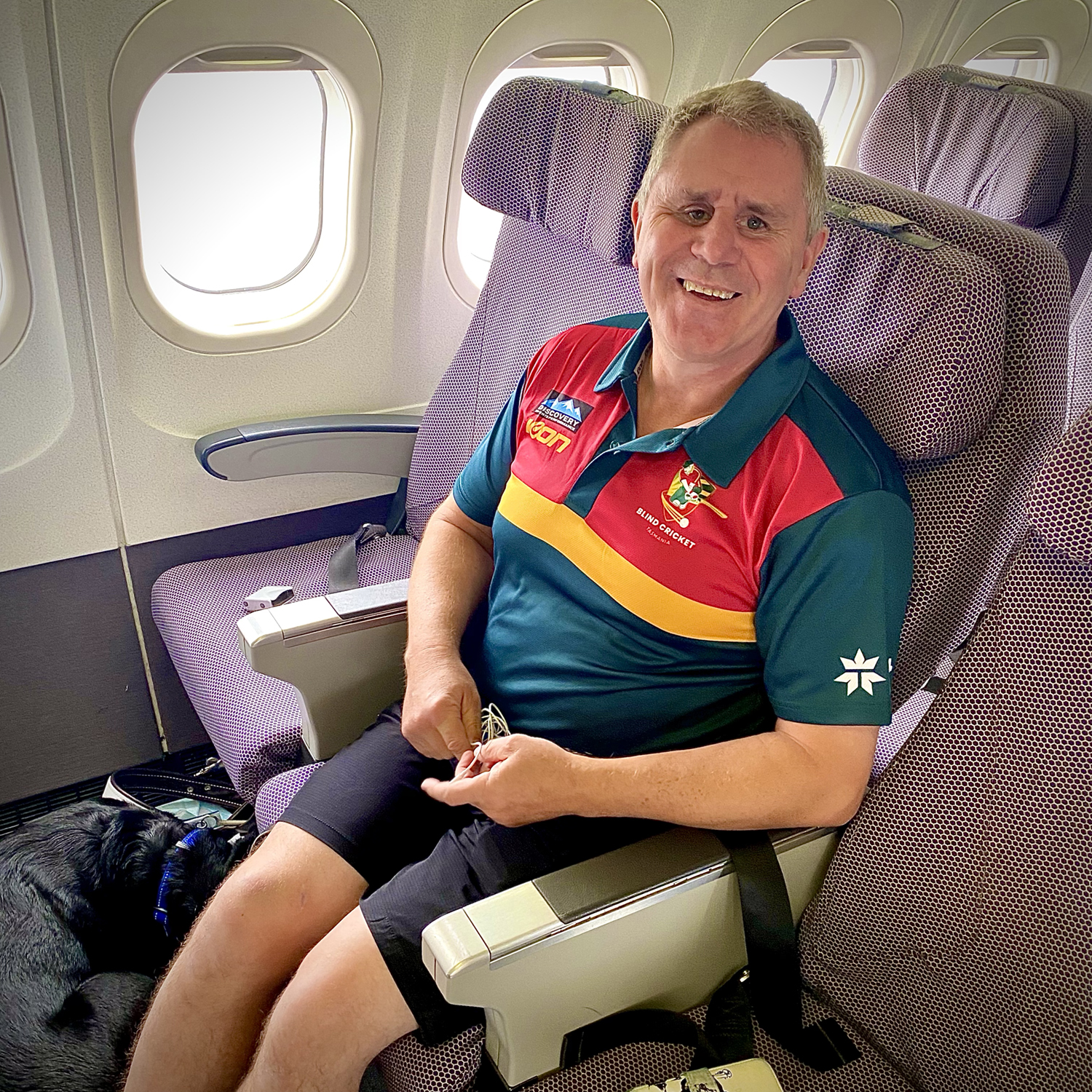 Phil Menzie and his guide dog 'Dudley' sitting in the front row of the plane on his way to the National Cricket Inclusion Championships with the other Tigers players