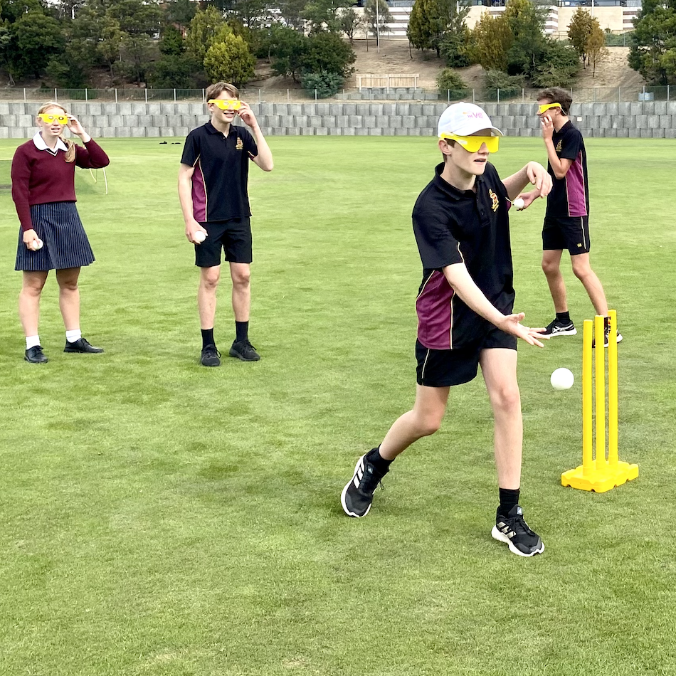 Young male Hutchins and female Collegiate high students wearing the simulation glasses learning to play blind cricket on the Hutchins oval